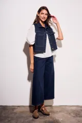 Chaleco de jean azul oscuro con cuello, bolsillos frontales y cierre con botones dorados. Corte al cuerpo.