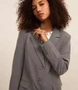 Blazer gris de poliéster, viscosa y elastano, de corte alargado, con cuello con solapas, bolsillos y cierre frontal con botones.