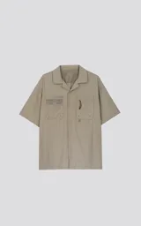 Camisa beige de manga corta, estilo técnica, confeccionada en microfibra liviana. Con doble bolsillo frontal y broches en lugar de botones.