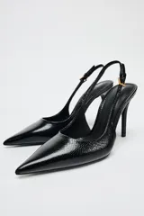 Zapato de tacón fino color negro con efecto relieve en el cuerpo, tira trasera con hebilla ajustable y acabado en punta.