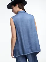 Camisa gris sin mangas confeccionada en viscosa teñida en frío, con efecto gastado. Tiene cuello clásico, cartera oculta y ruedo irregular más largo en los laterales.