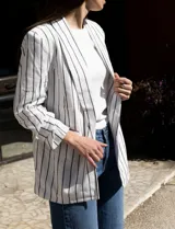 Blazer blanco con rayas verticales negras, cuello con solapa, bolsillos simulados y mangas 3/4 fruncidas. Forro interno blanco, marca Dictionary.