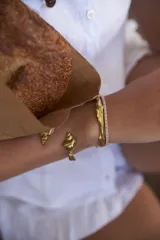 Brazalete rígido dorado con forma de caracola en los extremos.