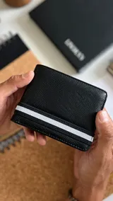 Billetera negra de símil cuero con galón elastizado blanco. Interior con doble repartición para billetes, visor y tarjeteros.