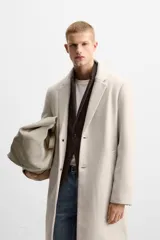 Abrigo recto color beige confeccionado en tejido con lana. Tiene cuello con solapas de muesca, manga larga con puños abotonados, bolsillos de vivo en la cadera, bolsillo interior, abertura en el centro de la espalda y cierre frontal con botonadura.