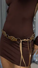 Cinturón marrón de cuero sintético con tachas plateadas y argollas metálicas.