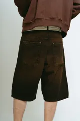 Bermuda de jean color marrón con lavado gastado, corte baggy, bolsillos grandes y bordados ornamentales en los laterales.