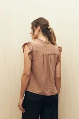 Camisa color beige con textura suave, cuello mao con volado y mangas cortas con pequeño volado. Presenta botonadura frontal.