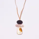 Colgante con cordón de gamuza color camel, compuesto por tres dijes apilados de forma orgánica: uno superior ovalado color marrón oscuro, uno central rectangular alargado color rosa pálido, y uno inferior irregular con vetas blancas y naranjas/doradas.