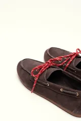 Mocasín tipo boat shoe con estampado de vaca en tonos marrón y blanco, confeccionado en cuero. Cuenta con cordones de cuero marrón oscuro y suela de goma.