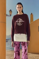 Buzo color bordó de corte cropped con mangas largas y cuello redondo. Presenta un estampado en el frente con texto y diseño gráfico.