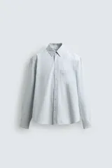 Camisa celeste a rayas verticales blancas, de corte relaxed fit, cuello solapa, manga larga con puños abotonados, bolsillo de parche en el pecho y cierre frontal con botones.