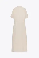 Vestido camisero largo color beige, de manga corta y cuello solapa. Tiene bolsillos de parche en el pecho, bolsillos laterales ocultos y cinturón de la misma tela.