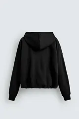 Sudadera negra con capucha, corte boxy, cierre frontal con cremallera, bolsillos laterales y puños elásticos.