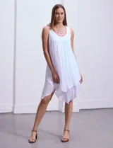 Vestido blanco de gasa con escote redondo bordado con apliques metálicos. Tiene forro interno a tono y ruedo en capas asimétricas.