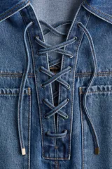Camisa popover de denim azul con costuras en color contrastante, corte oversized, hombros caídos, cuello abierto con detalle de cordón, bolsillos grandes superiores, mangas al codo y bajo levemente redondeado.
