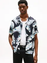 Camisa de hombre de corte regular con estampado de hojas en tonos azul y blanco sobre fondo negro. Tiene cuello cubano y manga corta.