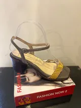 Sandalias de tacón Les Insolentes, color gris con detalles en amarillo y marrón. Tira delantera con estampado de piel de serpiente, tira al tobillo con hebilla y tacón cuadrado.