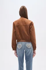 Campera estilo bomber corta de gamuza color marrón, con cuello redondo, cierre frontal de botones y dos bolsillos de parche con solapa en el pecho. Presenta puños y cintura elásticos.