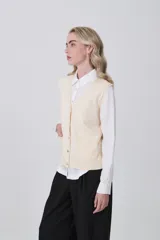 Chaleco de punto color crema, con cuello en V, cierre frontal de botones y dos bolsillos frontales.