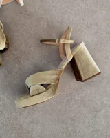 Sandalia de cuero vacuno color dorado, con plataforma y taco cuadrado. Presenta una tira delgada en el tobillo y detalle de nudo en la capellada.