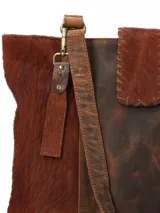 Bolso tote de cuero marrón con paneles de cuero peludo en los laterales y base de cuero liso. Tiene doble asa de hombro y correa bandolera ajustable y extraíble. El compartimento principal tiene cierre de cremallera y múltiples bolsillos interiores.