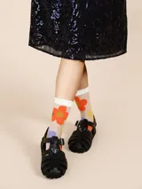 Medias de caña media transparentes con puño blanco con volados y estampado de flores rojas, amarillas y azules. Puntera y talón negros.