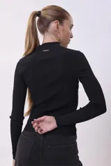 Blusa de punto negro con cuello alto y ajuste ceñido, de manga larga.