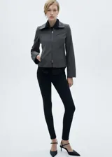 Chaqueta gris con finas rayas verticales, corte entallado, cuello camisero, cierre frontal con cremallera doble, bolsillo de ribete en el pecho y mangas largas.