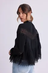 Blusa negra con cuello alto y mangas largas, con detalles de encaje en el pecho, mangas y ruedo.