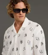 Camisa de manga corta para hombre, corte boxy, color blanco con cuello bowling y un estampado repetitivo de figuras geométricas negras.