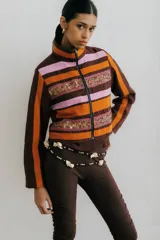 Chaqueta corta con cuello alto y cierre frontal con cremallera metálica. Diseño a rayas horizontales color crudo y verde, con galones bordados.