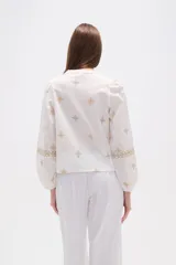 Blusa de algodón color tostado con bordados geométricos en blanco y azul marino, cuello mao con escote en V y mangas largas abullonadas con puños elásticos.