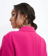 Campera color fucsia de crepe con cuello de camisa, manga abullonada, cierre frontal con botones y bolsillos frontales aplicados.