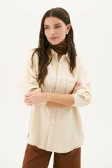 Camisa beige de corte recto, con cuello clásico, cierre frontal con botones, bolsillo en el pecho y mangas largas con puños abotonados.