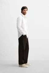 Camisa de vestir slim fit de algodón, color blanco con diseño de cuadros en tonos grises y beige. Tiene cuello italiano, mangas largas con puños abotonados y cierre frontal con botones.