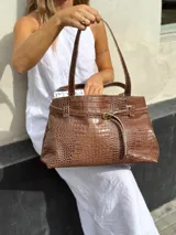 Bolso tote marrón con textura de cocodrilo, doble asa de hombro y cierre con cordón ajustable.