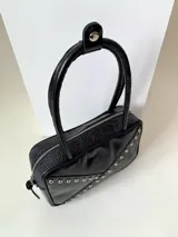 Cartera rígida negra de cuero con tachas plateadas y tres combinaciones de cuero diferentes que aportan textura. Tiene herrajes y cierre metálico plateado marca YKK. Cuenta con un asa fina para llevar al hombro o en la mano y una correa larga extra regulable.
