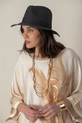 Vestido largo color natural con estampado de hojas de palmera en tonos verdes. Tiene corte amplio tipo túnica, cuello redondo, mangas tres cuartos, bolsillos laterales y ruedo con ribete.