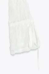 Top semitransparente de encaje blanco, con cuello redondo y mangas largas acampanadas con volantes ajustables con lazada.
