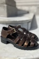 Sandalias de cuero color cobre con diseño de tiras entrecruzadas, hebilla lateral y suela track color negro.