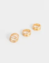 Set de tres anillos dorados de metal con diferentes diseños: uno con tres aros abiertos, otro con tres aros lisos y otro con dos aros lisos.