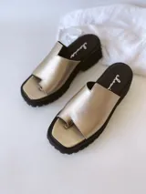 Sandalias doradas con tira para el dedo y suela track negra.