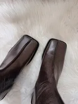 Botas cortas color chocolate con textura de cocodrilo, punta cuadrada y tacón bajo. Cuentan con cierre lateral.