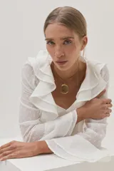 Blusa blanca de gasa con lunares, escote en V con volados y mangas largas acampanadas.
