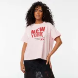 Camiseta rosa de corte amplio con estampado de texto en rojo que dice "New York, Sleepless Nights and City Lights" y dos estrellas.