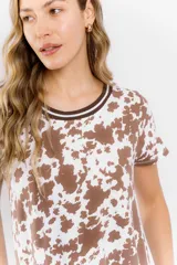 Vestido blanco con estampado de manchas marrones tipo vaca, corte recto y cuello redondo con ribete marrón.