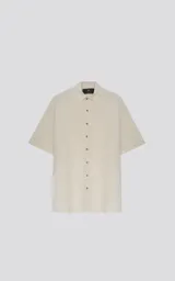 Camisa oversize color crema con cuello clásico, cierre frontal con botones marrones y mangas cortas.