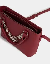 Cartera tipo city de cuerina color bordó, con doble asa corta y correa larga regulable. Incluye charm decorativo con cadena plateada y dijes colgantes.