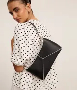 Cartera baguette mediana de cuero sintético color negro, con recortes geométricos en blanco en el frente y asa corta con detalle metálico.